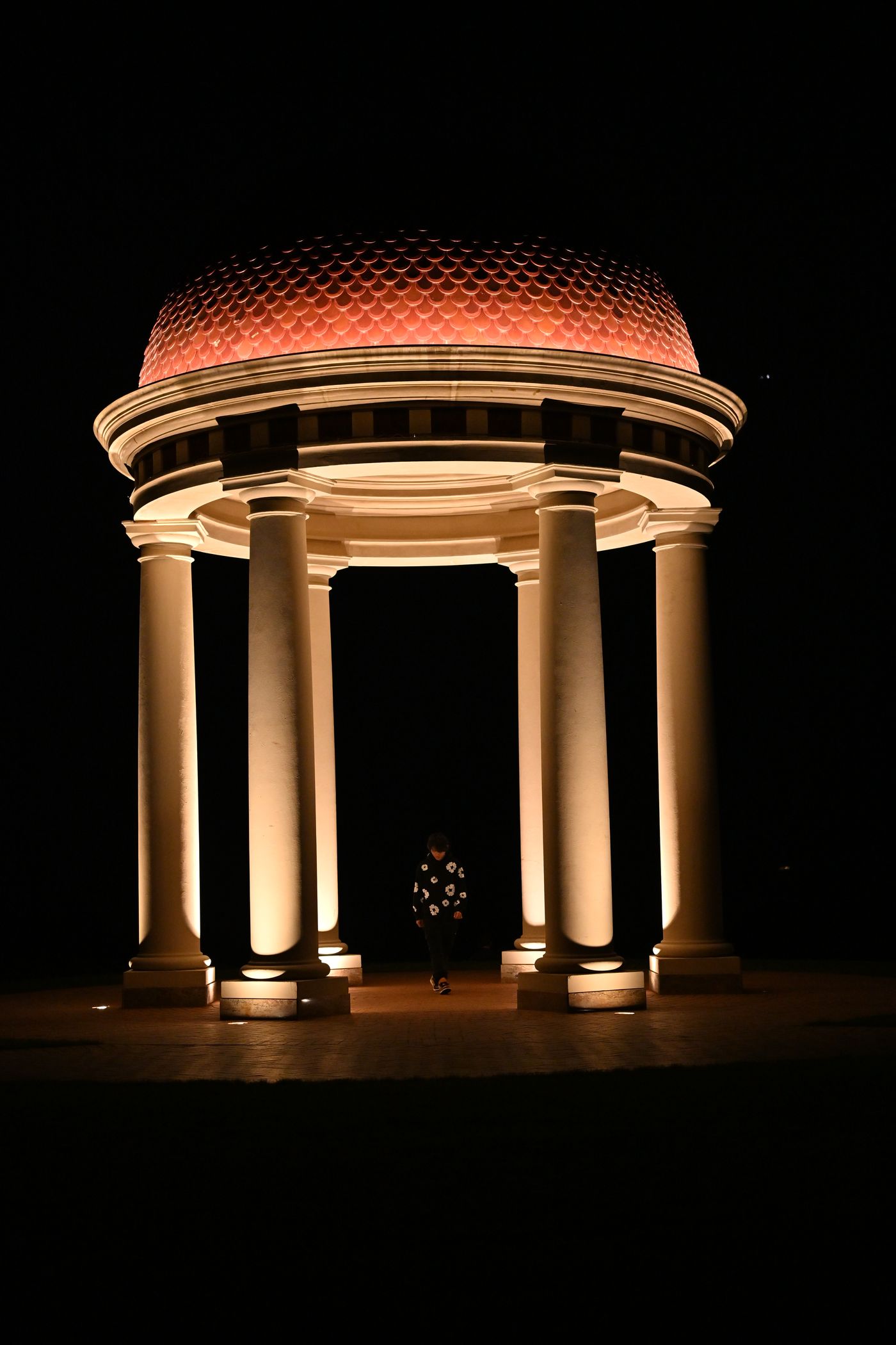 A lit neoclassical rotunda at night, one figure standing beneath the dome